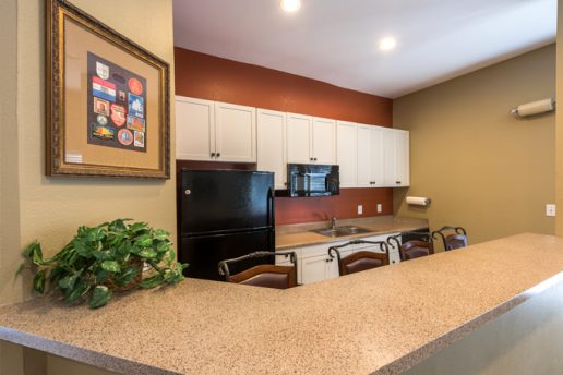 Kitchen with black refrigerator, burnt orange wall, tan wall, white cabinets, cream countertops, breakfast bar