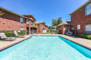 Exterior Swimming pool, fenced in, red brick buildings, lush foliage, meticulous landscaping, photo taken on a sunny day.