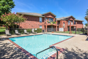 Exterior Swimming pool, fenced in, red brick buildings, lush foliage, meticulous landscaping, photo taken on a sunny day.